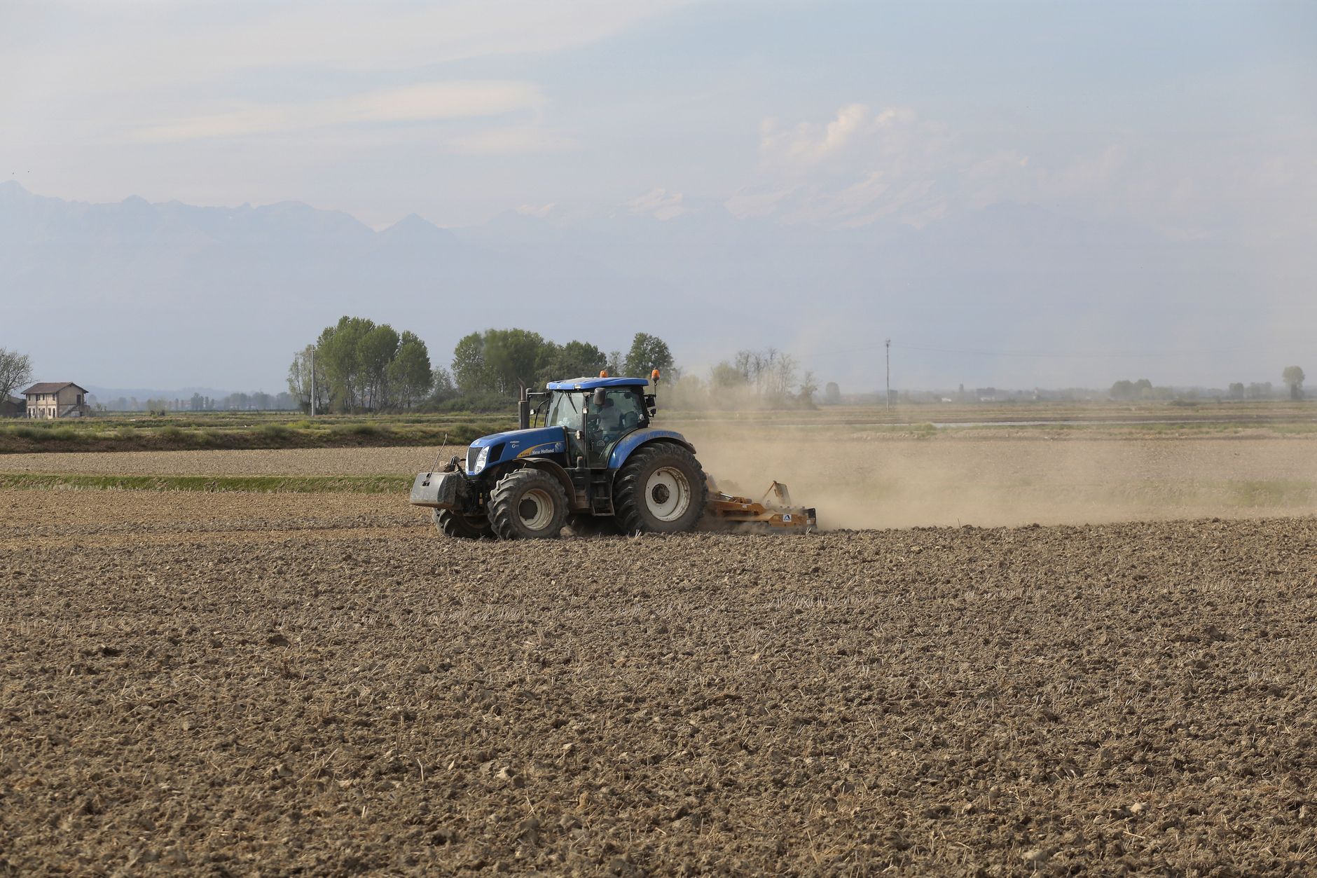 A farmer kneeling in a tilled field examining a handful of dark soil