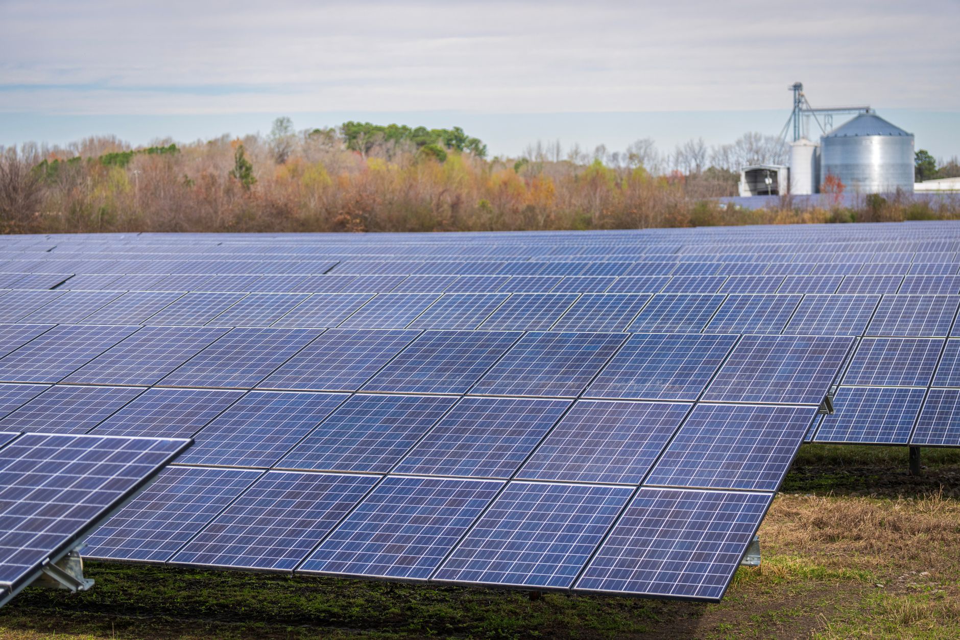 Solar panels installed in rows across an open farm field with tilled soil visible between the rows